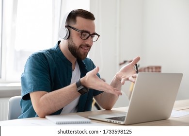 Smiling businessman in headphones looking at laptop screen watching webinar. Happy young bearded man have break at work relaxing distance learning languages. Manager watching training video concept.