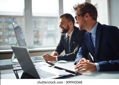 Smiling Businessman And His Colleague Looking At Computer Monitor At Meeting