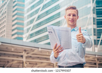 Smiling businessman holding newspaper and showing thumb up on outside street city