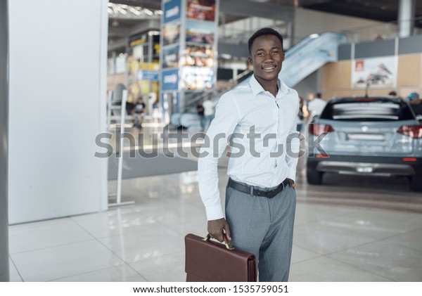 Smiling\
businessman holds briefcase, car\
showroom