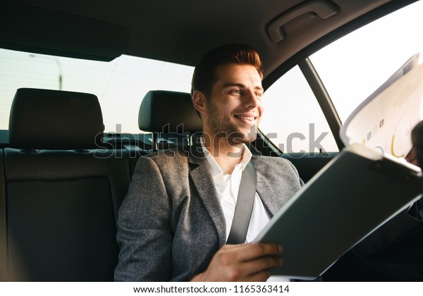 Smiling businessman looking through documents while\
sitting at the back of a\
car