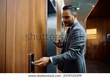 Smiling businessman pressing elevator button in a lobby.