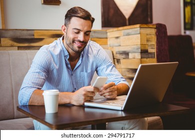 Smiling businessman sending a text message with laptop beside at the cafe - Powered by Shutterstock