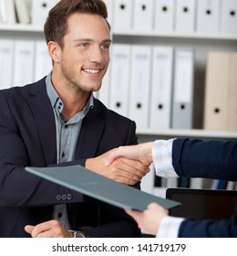 Smiling businessman shaking hands with a cropped female interviewer in office