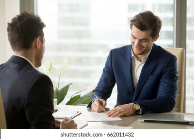 Smiling businessman signing paper at meeting, satisfied entrepreneur concludes contract, holder verifies agreement by putting authorized handwritten signature, entrepreneur making profitable deal