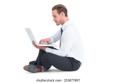 Smiling businessman sitting on floor using laptop on white background