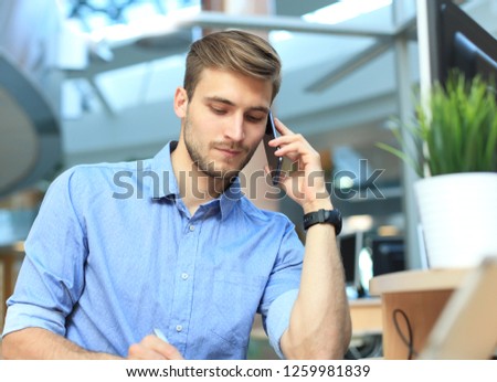 Smiling businessman sitting and using mobile phone in office.