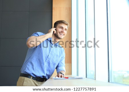 Smiling businessman standing and using mobile phone in office.