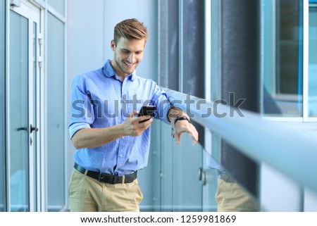 Smiling businessman standing and using mobile phone in office.