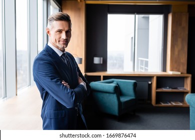 smiling businessman in suit with crossed arms looking at camera in hotel