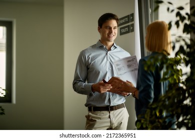 Smiling Businessman Talking To Female Coworker In A Hallway Of An Office Building. Copy Space.