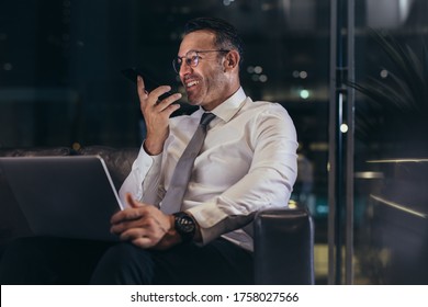 Smiling Businessman Talking On Phone At Airport Lounge With A Laptop. Man Waiting Of His Flight At Airport Terminal And Talking On Cell Phone.