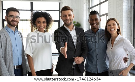 Smiling businessman team leader offering hand for handshake, standing with successful colleagues in modern office, friendly hr manager standing with extended hand, welcoming new workers at job