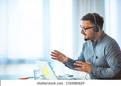 Smiling businessman using headset when talking to customer. Tech support manager in headset consulting a client. Happy young male customer support executive working in office.