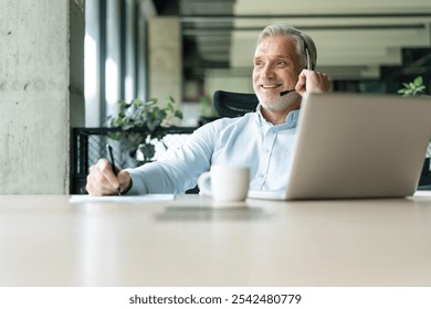 Smiling businessman using headset when talking to customer. Tech support manager in headset consulting a client. Happy mature male customer support executive working in office. - Powered by Shutterstock