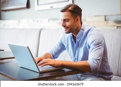 Smiling businessman using his laptop at the cafe - Powered by Shutterstock