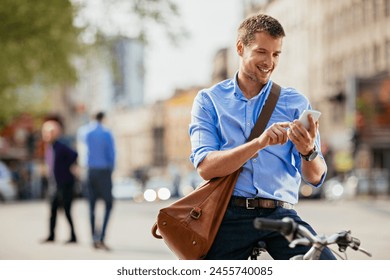 Smiling businessman using smartphone while leaning on bicycle in urban setting