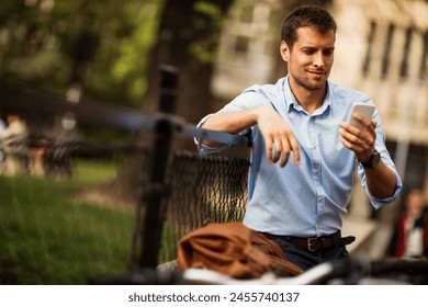 Smiling businessman using smartphone while leaning on bicycle in urban setting
