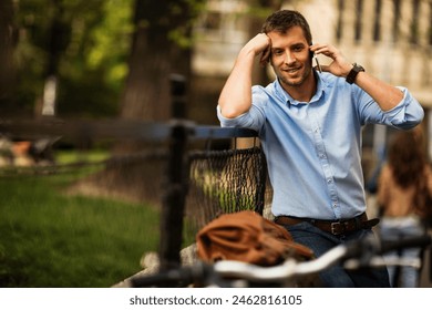Smiling businessman using smartphone while leaning on bicycle in urban setting