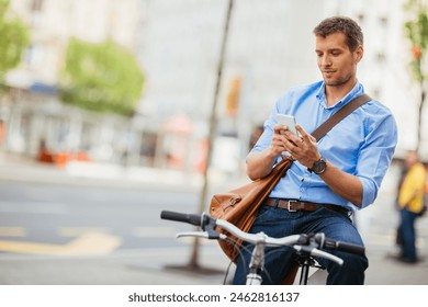 Smiling businessman using smartphone while leaning on bicycle in urban setting