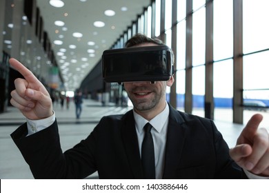 Smiling Businessman In VR Headset Enjoying Exploring Visualized Virtual Reality World In Business Center Lobby