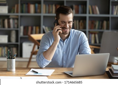 Smiling businessman wearing glasses talking on phone, sitting at desk with laptop, friendly manager consulting customer by phone, happy man chatting with friends distracted from work