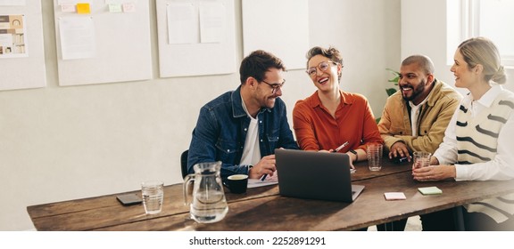 Smiling businesspeople having a discussion using a laptop in a creative office. Group of happy businesspeople sharing ideas while working together on a new interior design project. - Shutterstock ID 2252891291