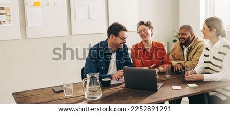 Smiling businesspeople having a discussion using a laptop in a creative office. Group of happy businesspeople sharing ideas while working together on a new interior design project.