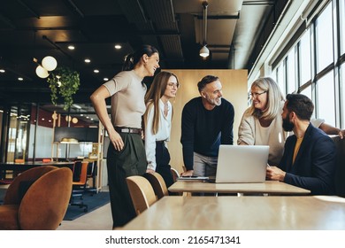 Smiling businesspeople having a discussion while collaborating on a new project in an office. Group of happy businesspeople using a laptop while working together in a modern workspace.