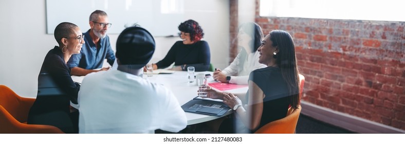 Smiling businesspeople sitting together in a meeting room. Group of successful businesspeople attending their morning briefing in a modern office. Cheerful colleagues working together. - Shutterstock ID 2127480083