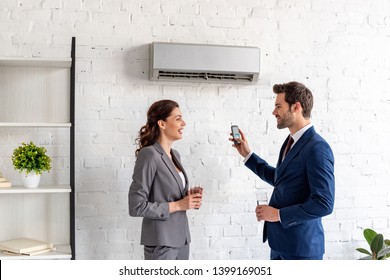 Smiling Businesspeople Talking While Standing Under Air Conditioner In Office