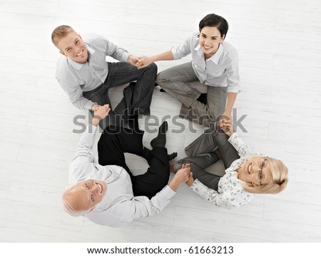 Smiling businessteam doing relaxation, looking at camera sitting on floor in lotus posture, high angle view.?