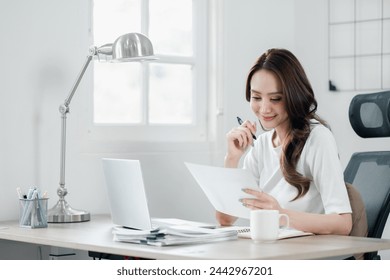 Smiling businesswoman in a bright office reviewing documents with a pen in hand, showing efficiency and focus in her professional routine. - Powered by Shutterstock