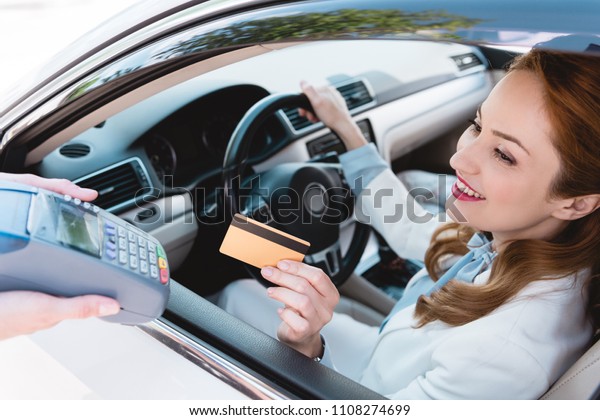 smiling businesswoman in car making payment with\
credit card