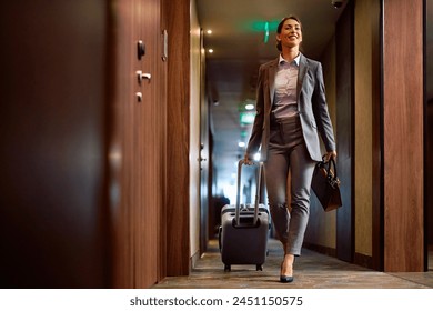 Smiling businesswoman with carry on luggage walking through hotel hallway. Copy space. - Powered by Shutterstock