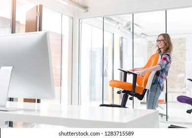 Smiling Businesswoman Carrying Orange Chair In New Office