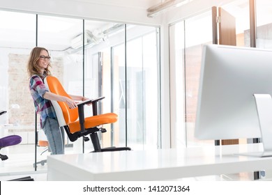 Smiling Businesswoman Carrying Orange Chair In New Office