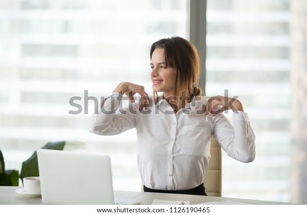 Smiling businesswoman doing easy office\
exercises to relieve neck and shoulder muscle tension from\
sedentary computer work, young employee taking break stretching for\
back relaxation at\
workplace