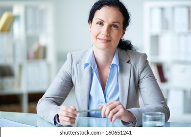 Smiling businesswoman in formalwear sitting at workplace in office