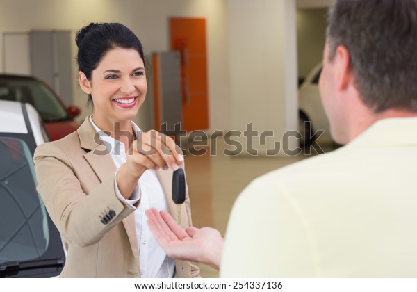 Smiling businesswoman giving car key to happy\
customer at new car\
showroom