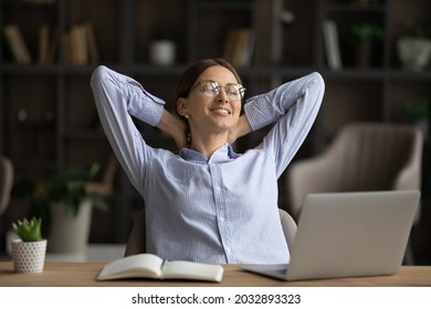 Smiling businesswoman in glasses relaxing at workplace after work done, young woman student leaning back with hands behind head in comfortable chair, sitting at desk with laptop, finished project