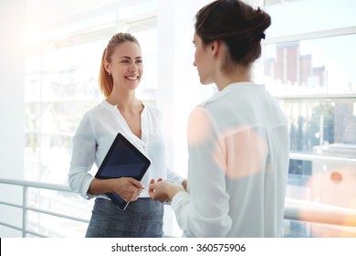 Smiling Businesswoman Holding Digital Tablet And Talking With Partner While Standing In Modern Office Interior, Team Of Professional Employees Discussing Ideas Of Project After Working On Touch Pad