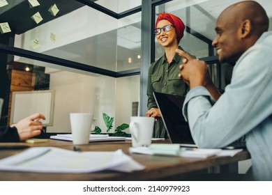 Smiling Businesswoman Leading A Meeting With Her Colleagues In A Boardroom. Muslim Businesswoman Sharing Creative Ideas With Her Team. Team Leader Wearing A Headscarf In A Multicultural Workplace.