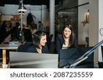 Smiling businesswoman listening to a collegue, in front of a computer, at desk, in office. They are in smart casuals.