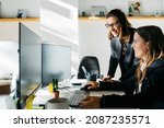 Smiling businesswoman listening to a collegue, in front of a computer, at desk, in office. They are in smart casuals.