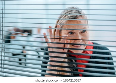 Smiling Businesswoman Looking Through Office Window Blinds.