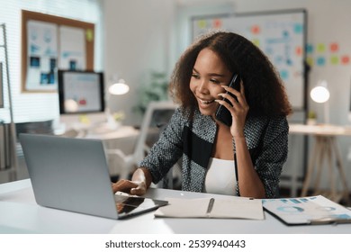 Smiling businesswoman multitasking, talking on mobile phone and working on laptop, enjoying productive workday in modern office - Powered by Shutterstock