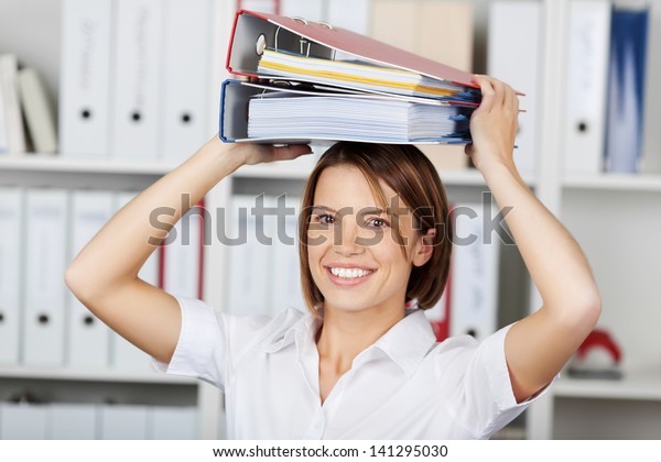 Smiling\
businesswoman or office worker wearing a bright white blouse\
holding a stack of file folders over her\
head