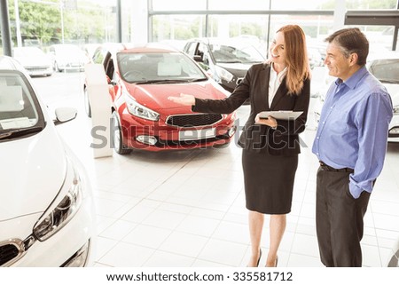 Smiling businesswoman showing car to customer at new car showrom