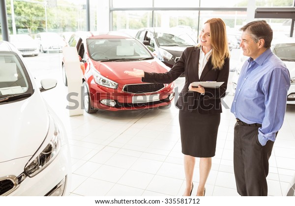 Smiling businesswoman showing car to customer at\
new car showrom